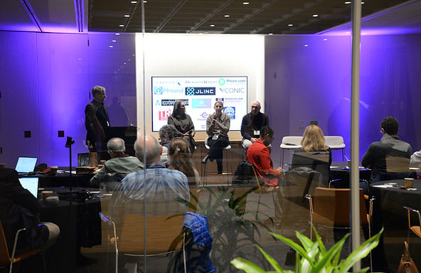 A purple-lit room with a panel on stage and attendees seated at tables